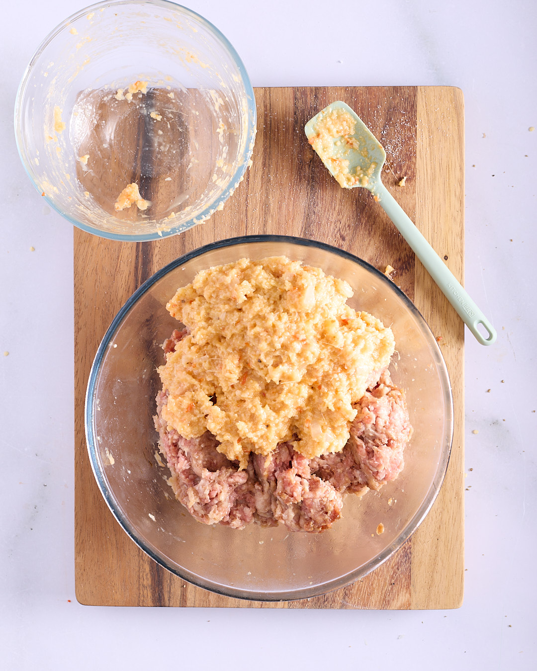 Aromatic breadcrumb mixture being added to seasoned ground pork and chicken mince in a glass bowl ready to combine for Vietnamese-style pork and chicken meatloaf.
