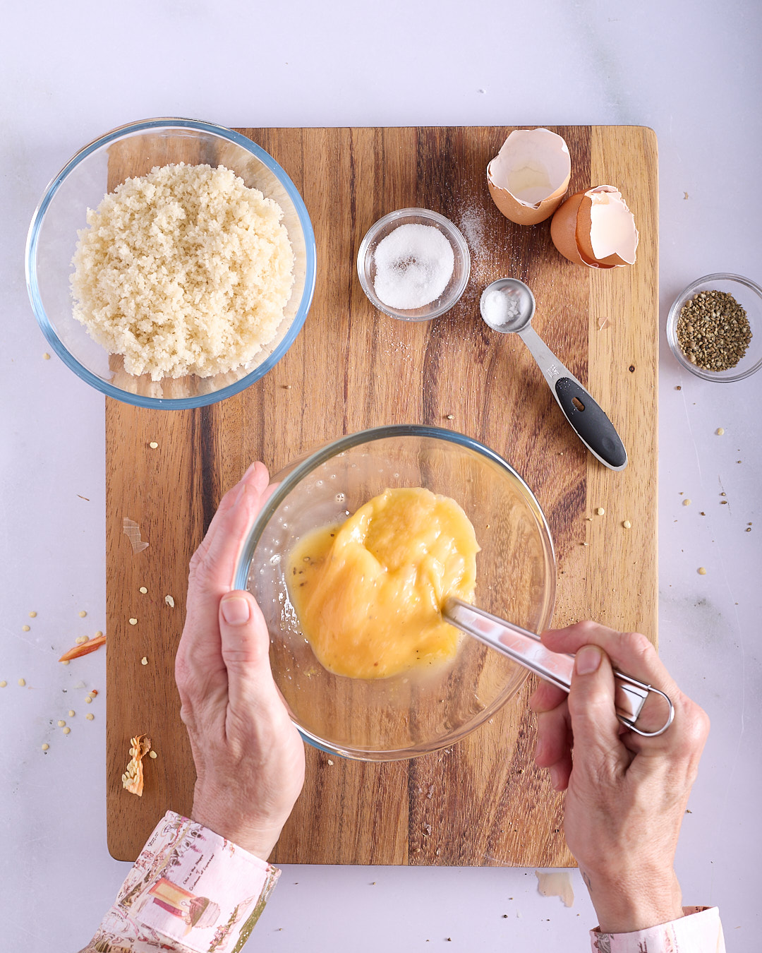 Sandra beating eggs in a glass bowl alongside fresh breadcrumbs, sugar and white pepper on a wooden board showing the egg mixture step for Vietnamese-style pork and chicken meatloaf.