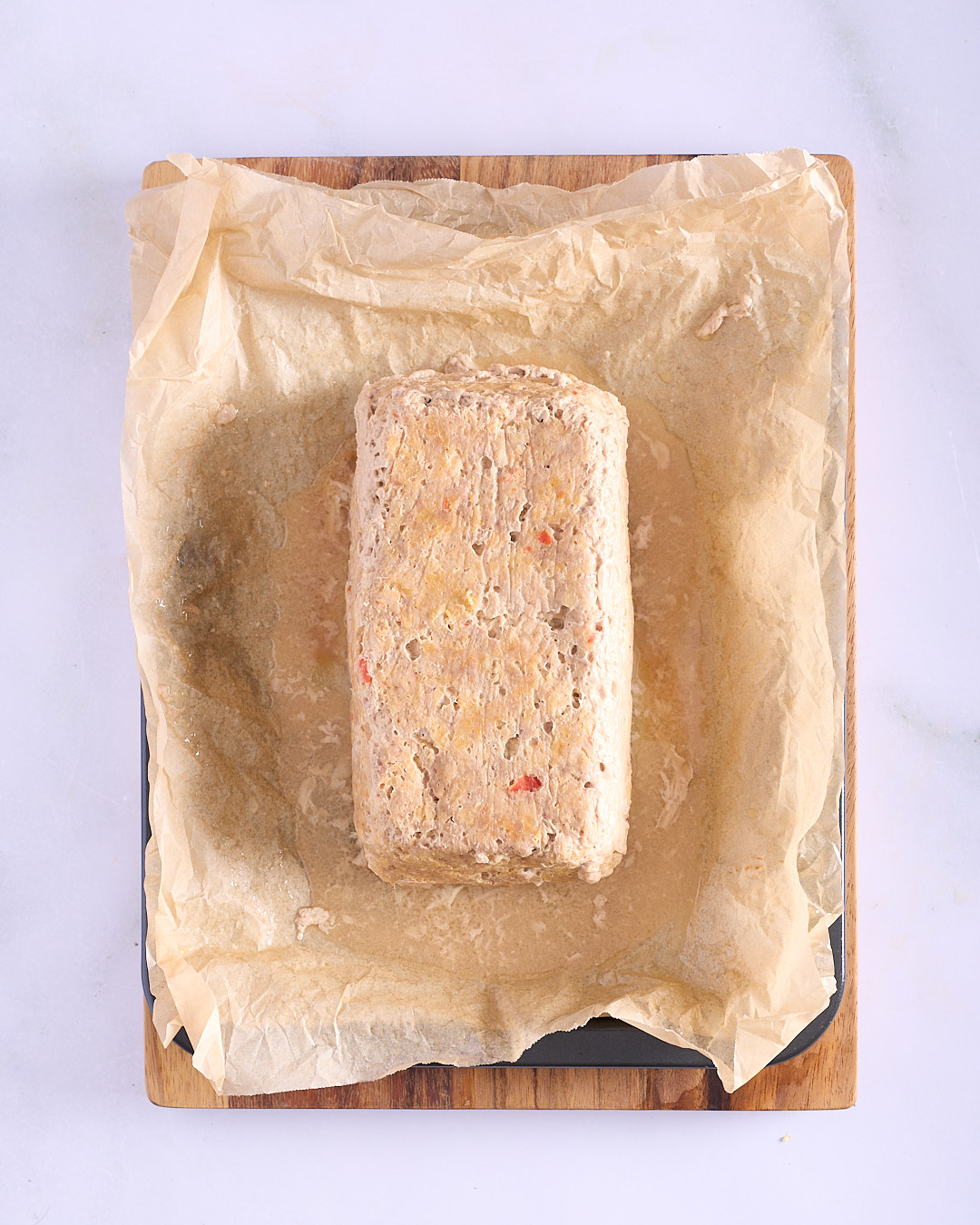 Vietnamese-style pork and chicken meatloaf turned out upside down onto baking paper on a rimmed baking sheet after the first bake, showing the compact set texture before glazing.
