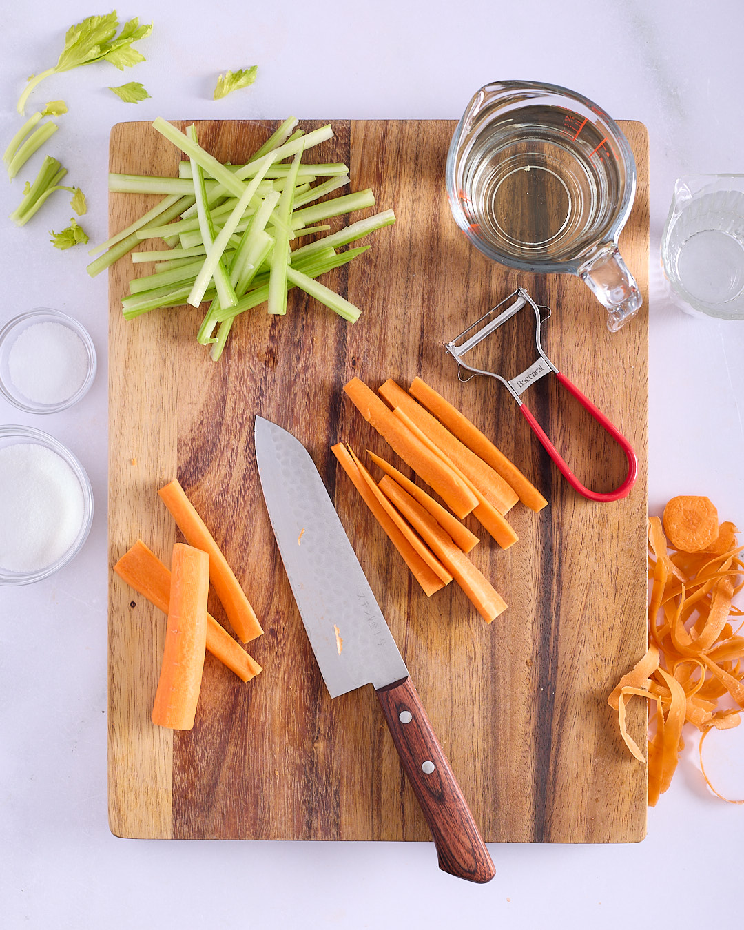 Carrot and celery cut into batons on a wooden chopping board with rice wine vinegar, salt and sugar alongside, showing the preparation of quick pickled vegetables for Vietnamese-style pork and chicken meatloaf bánh mì.