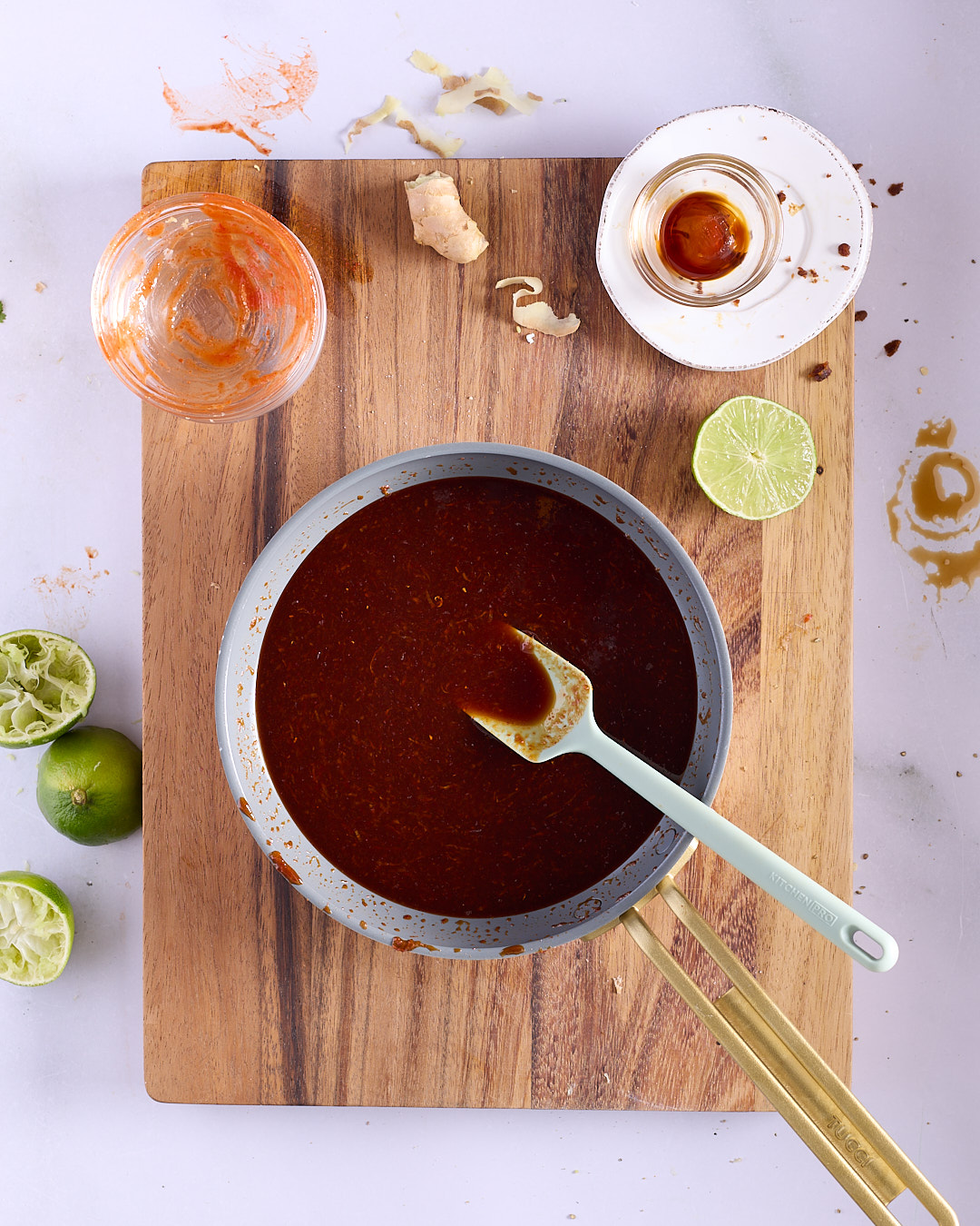 Sriracha palm sugar glaze simmering in a small saucepan with squeezed limes, ginger and fish sauce alongside on a wooden board, showing the glaze preparation step for Vietnamese-style pork and chicken meatloaf bánh mì.