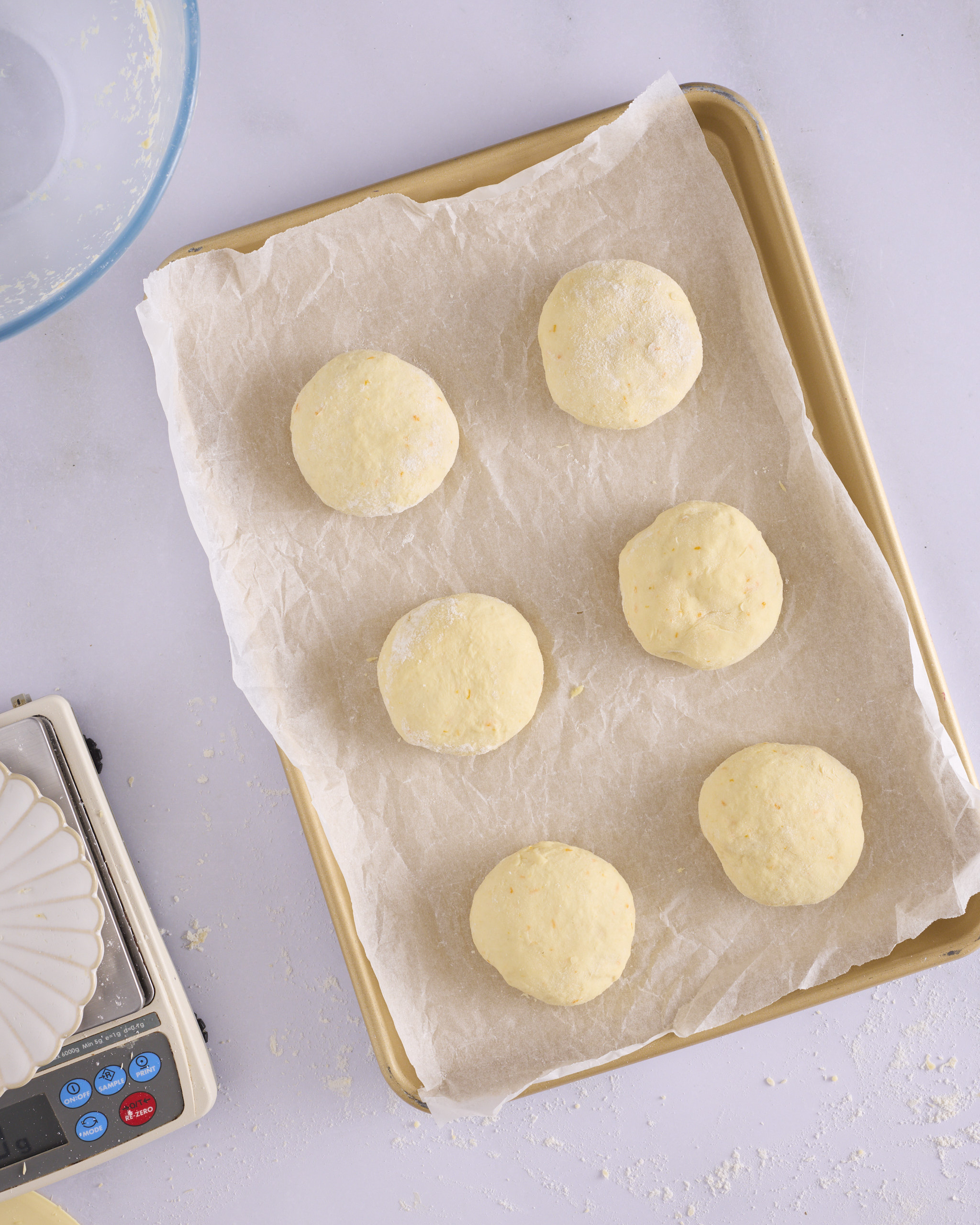 Six shaped and flattened dough discs for blueberry cheesecake kolache spaced in two rows of three on a gold baking tray lined with baking paper, ready to prove.