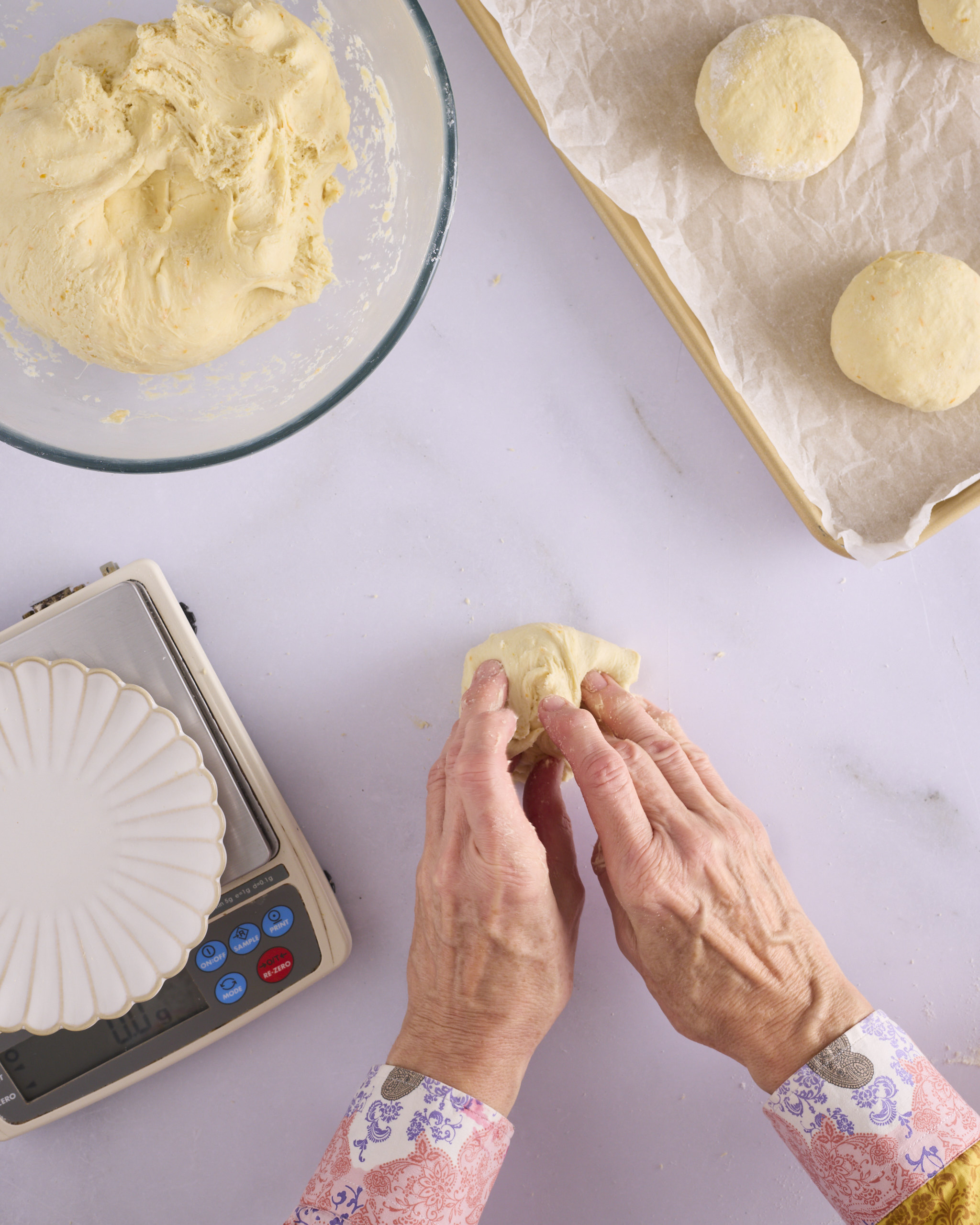 Sandra presses the stretched dough back into the centre of the 100g ball for blueberry cheesecake kolache, with the bowl of dough and a lined tray of shaped balls nearby.