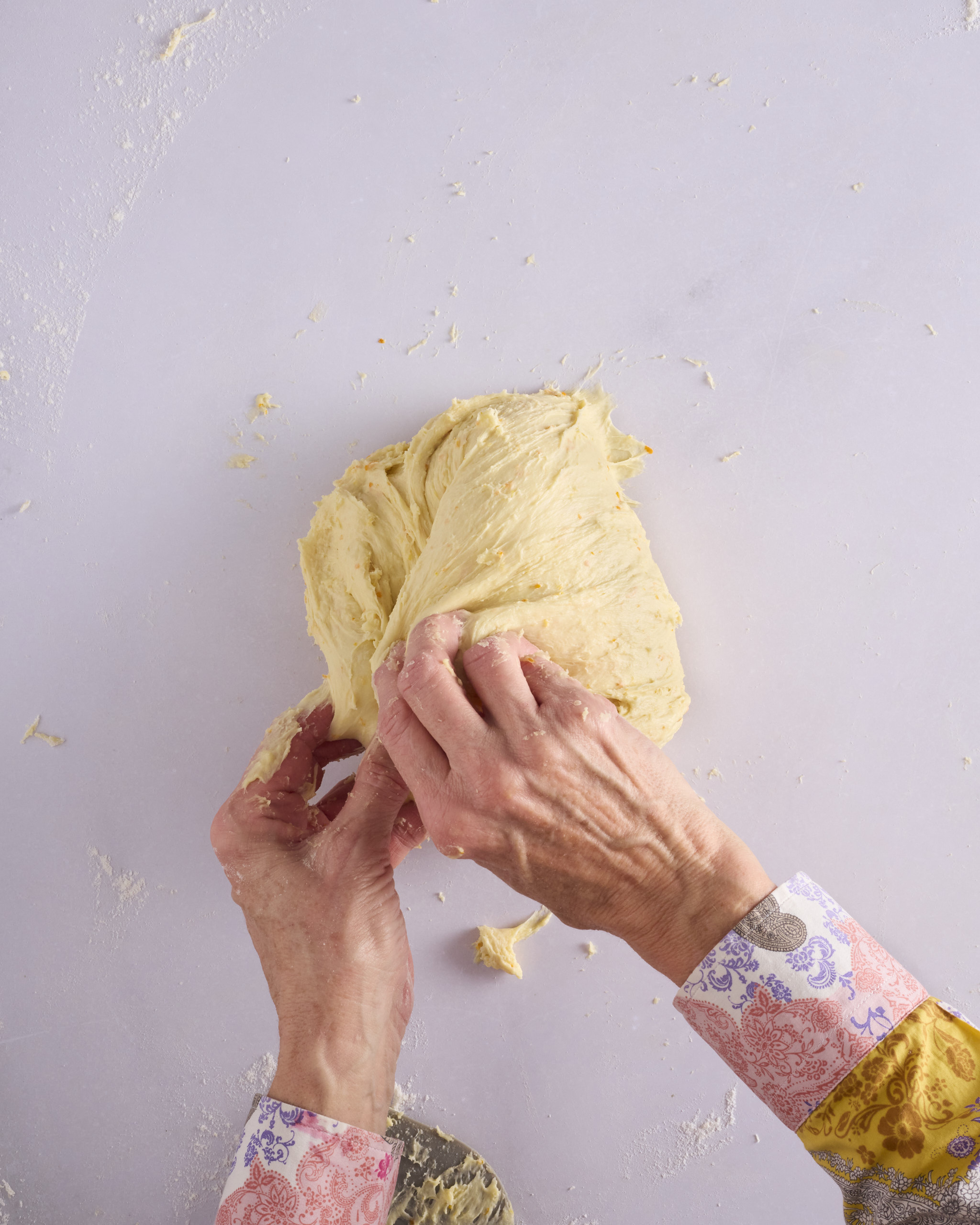 Sandra pinches a stretched piece of the foundation sweet dough into the centre of the forming ball. The dough is pale gold and slack, sitting on a lightly floured bench.