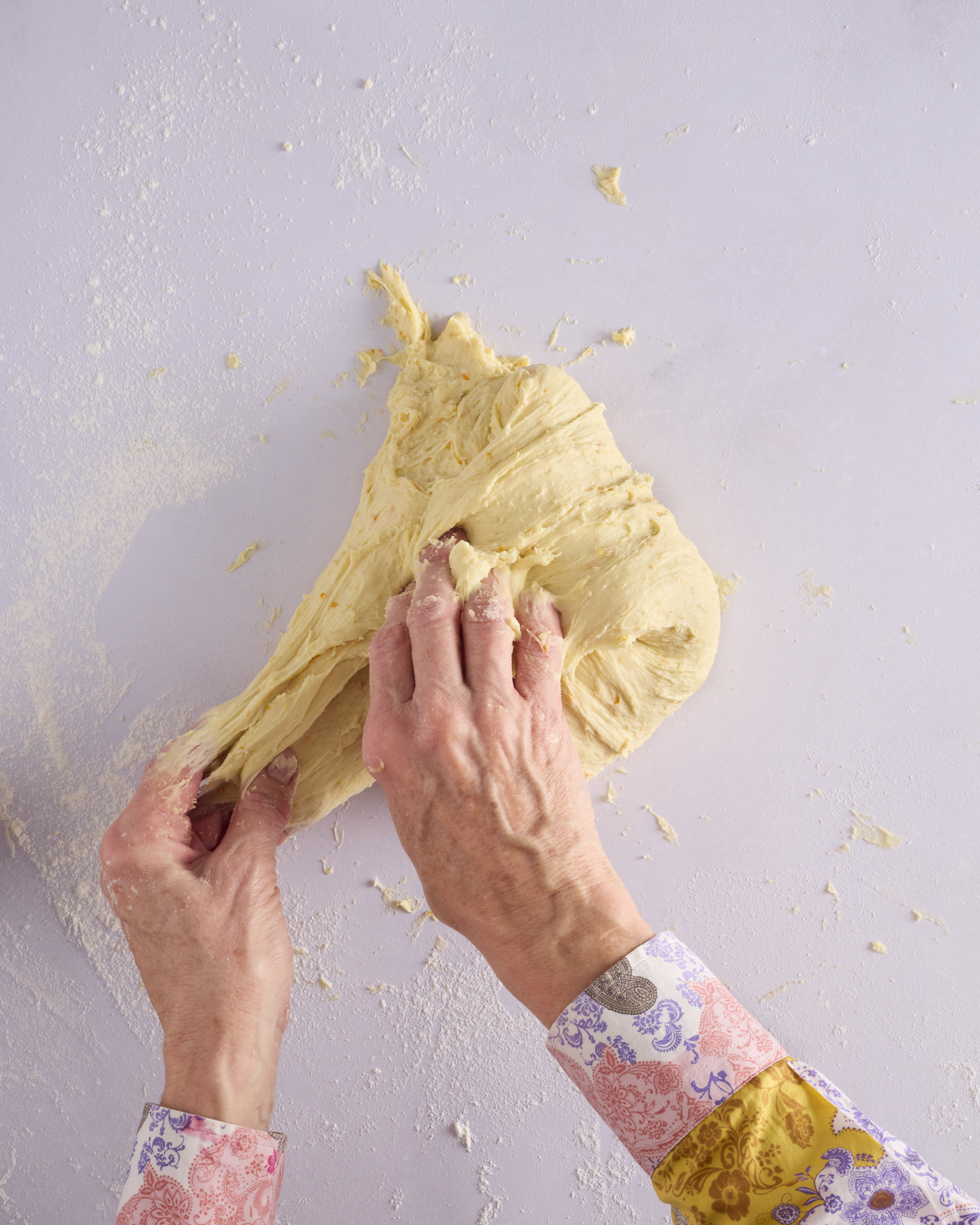 Sandra stretches a handful of the foundation sweet dough out across a floured bench. The dough is soft and elastic with flecks of orange zest, pulling into long strands as it stretches.